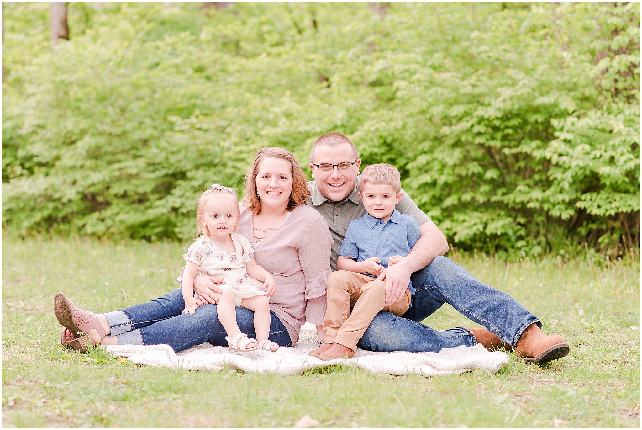 Family of four sitting on the grass smiling at the camera during their Northwest Park Annex family session