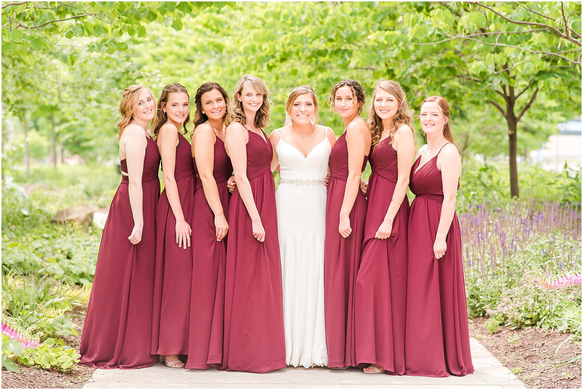 Bride in white wedding gown and bridesmaids in wine red dresses smiling at the camera during a wedding at The Phoenix Cincinnati