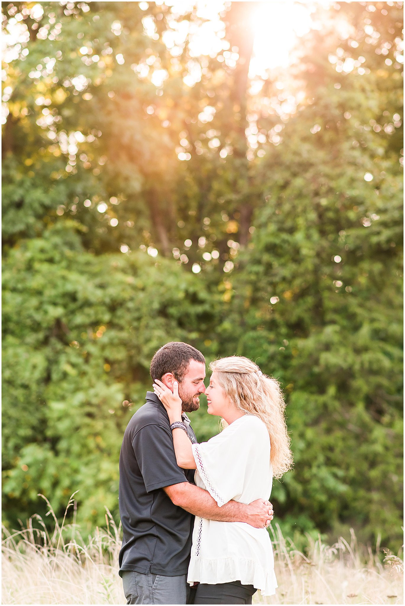 Bloomfield Indiana engagement session couple smiling at each other while standing in field at sunset