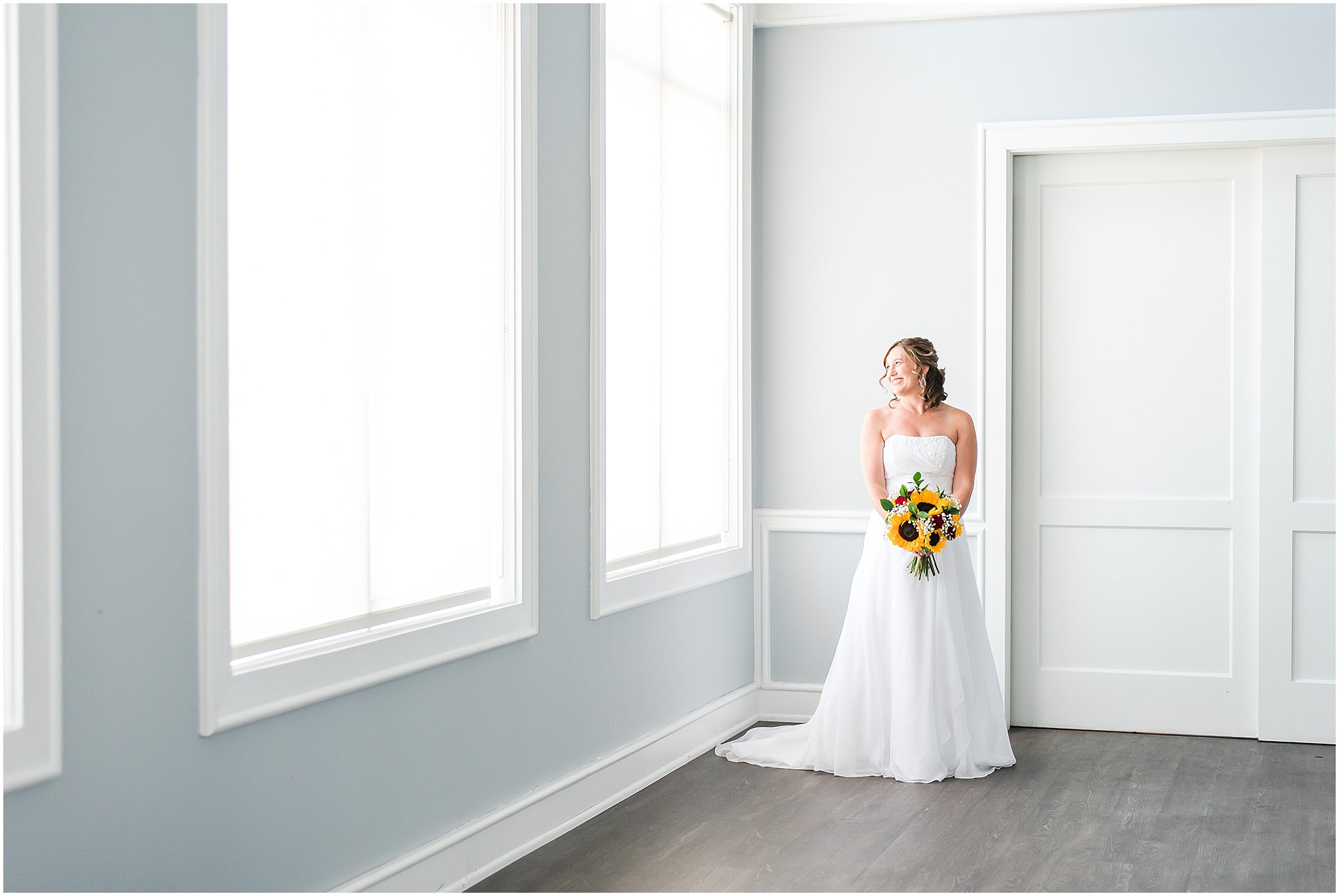 Bride holding sunflower and red rose bouquet next to window at The Hawthorns Golf and Country Club