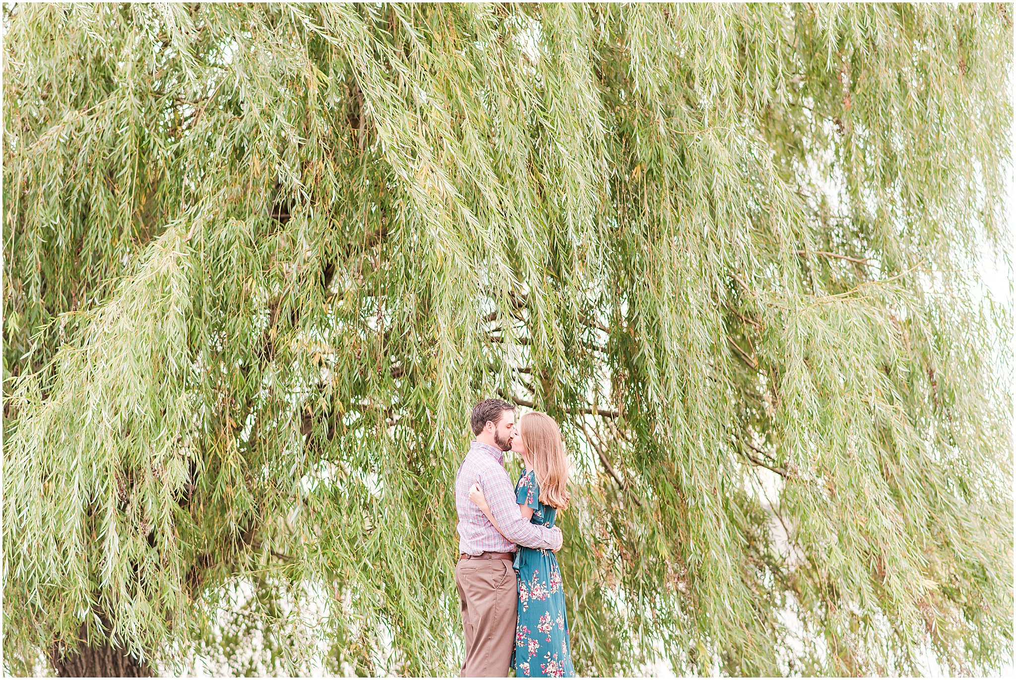 Bride and groom kissing in front of willow tree during Coxhall Gardens engagement session