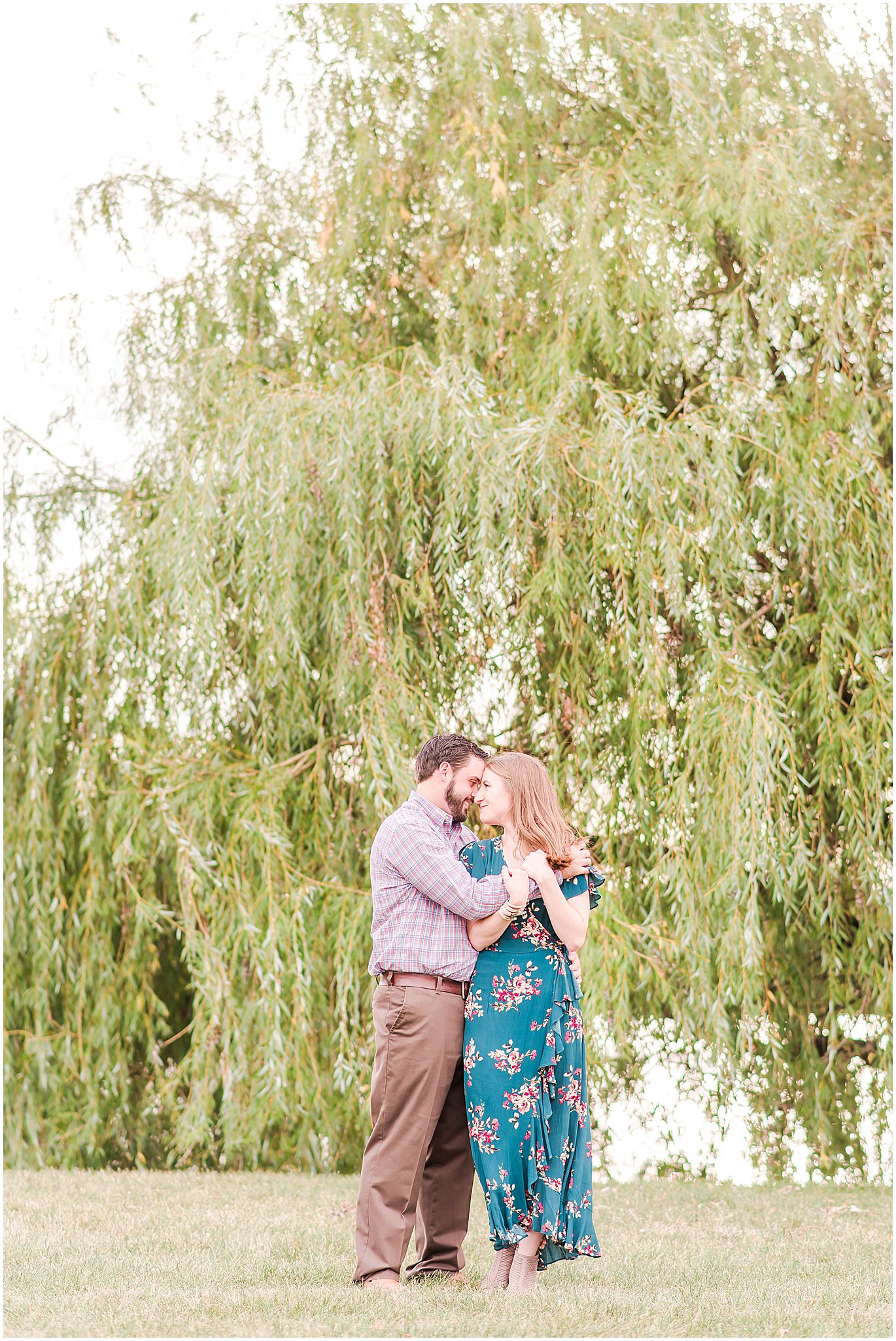 Bride and groom nuzzling in front of willow tree during Coxhall Gardens engagement session