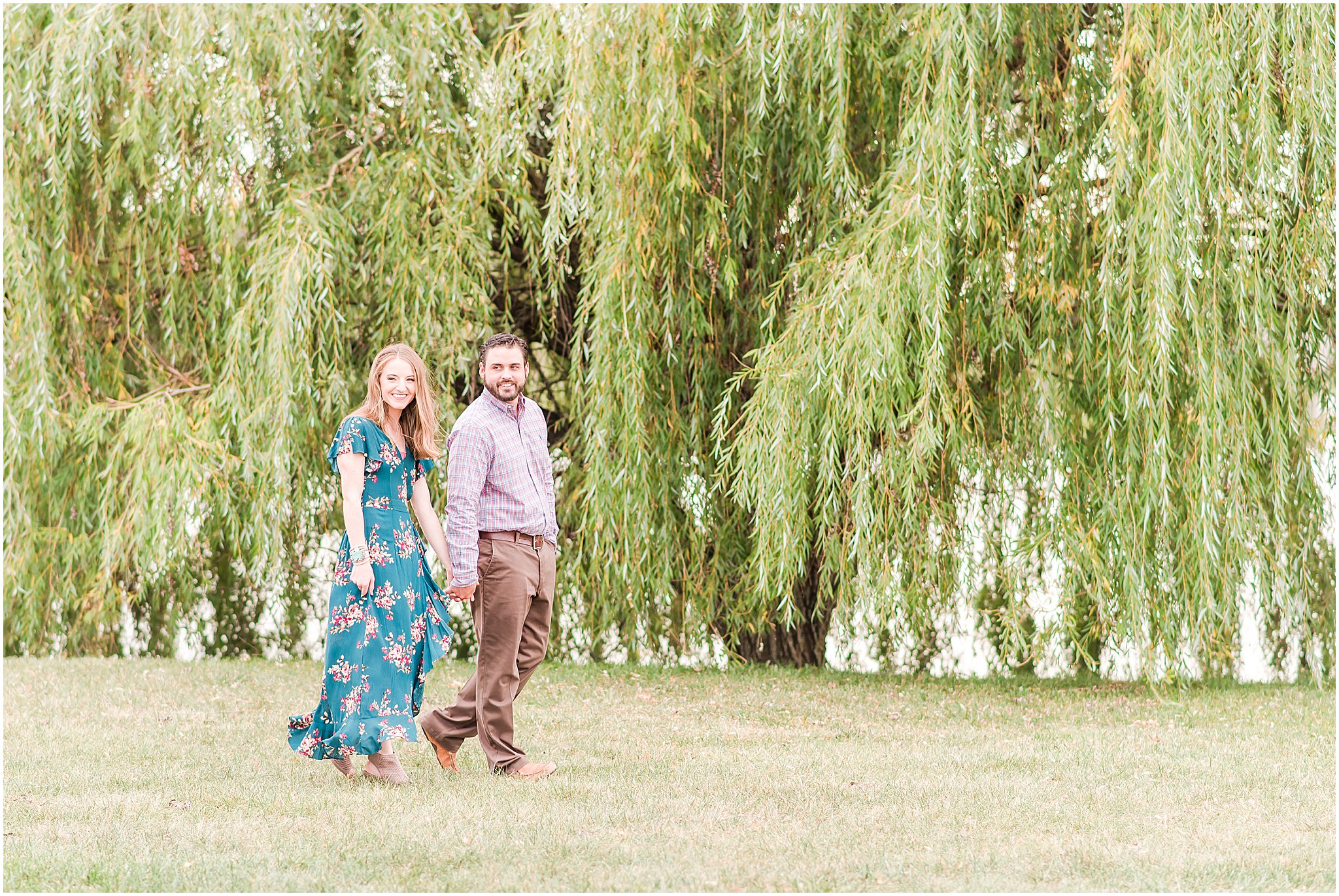 Bride and groom holding hands and walking in front of willow tree during Coxhall Gardens engagement session