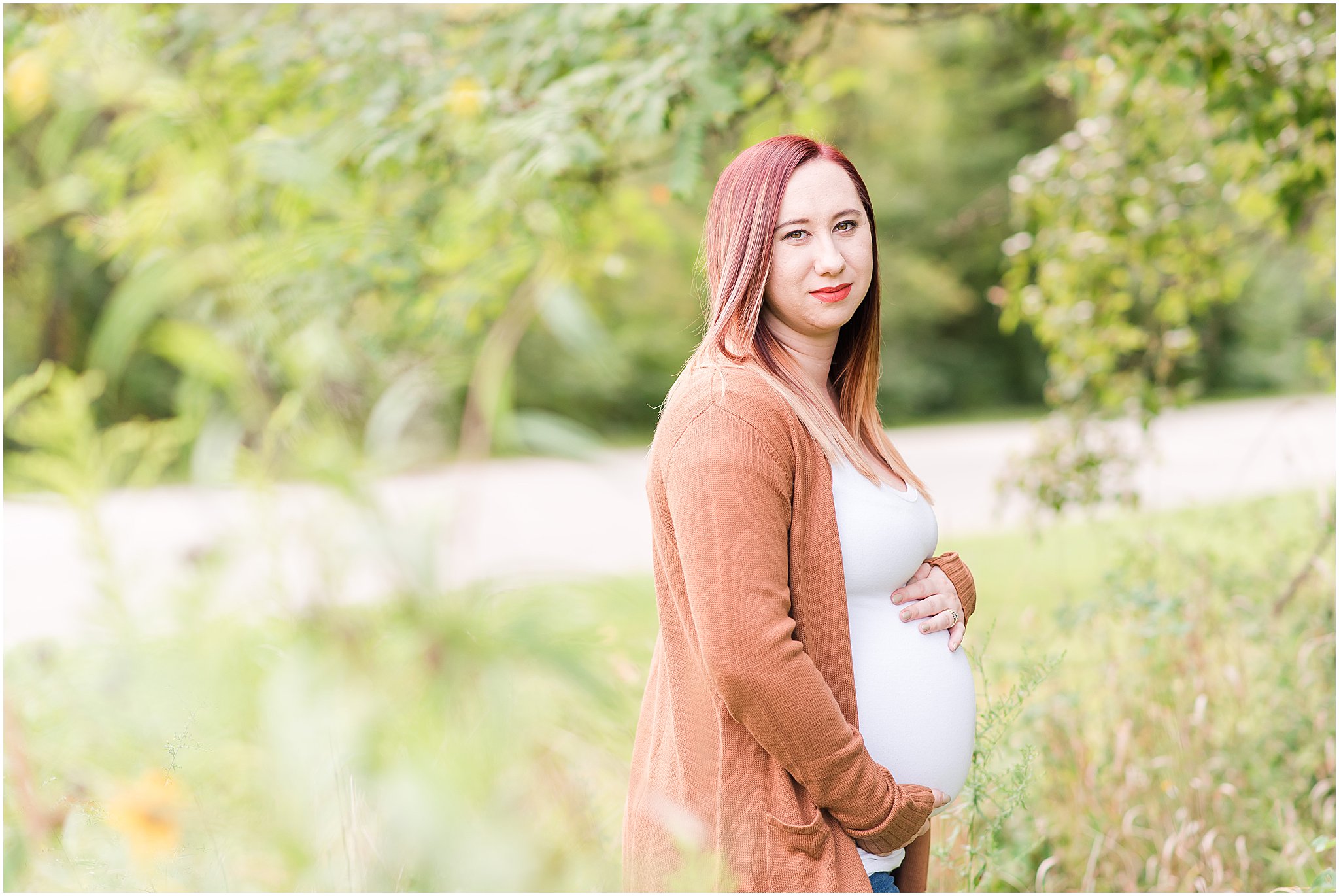 Pregnant woman holding belly and smiling at camera during Eagle Creek Park maternity session