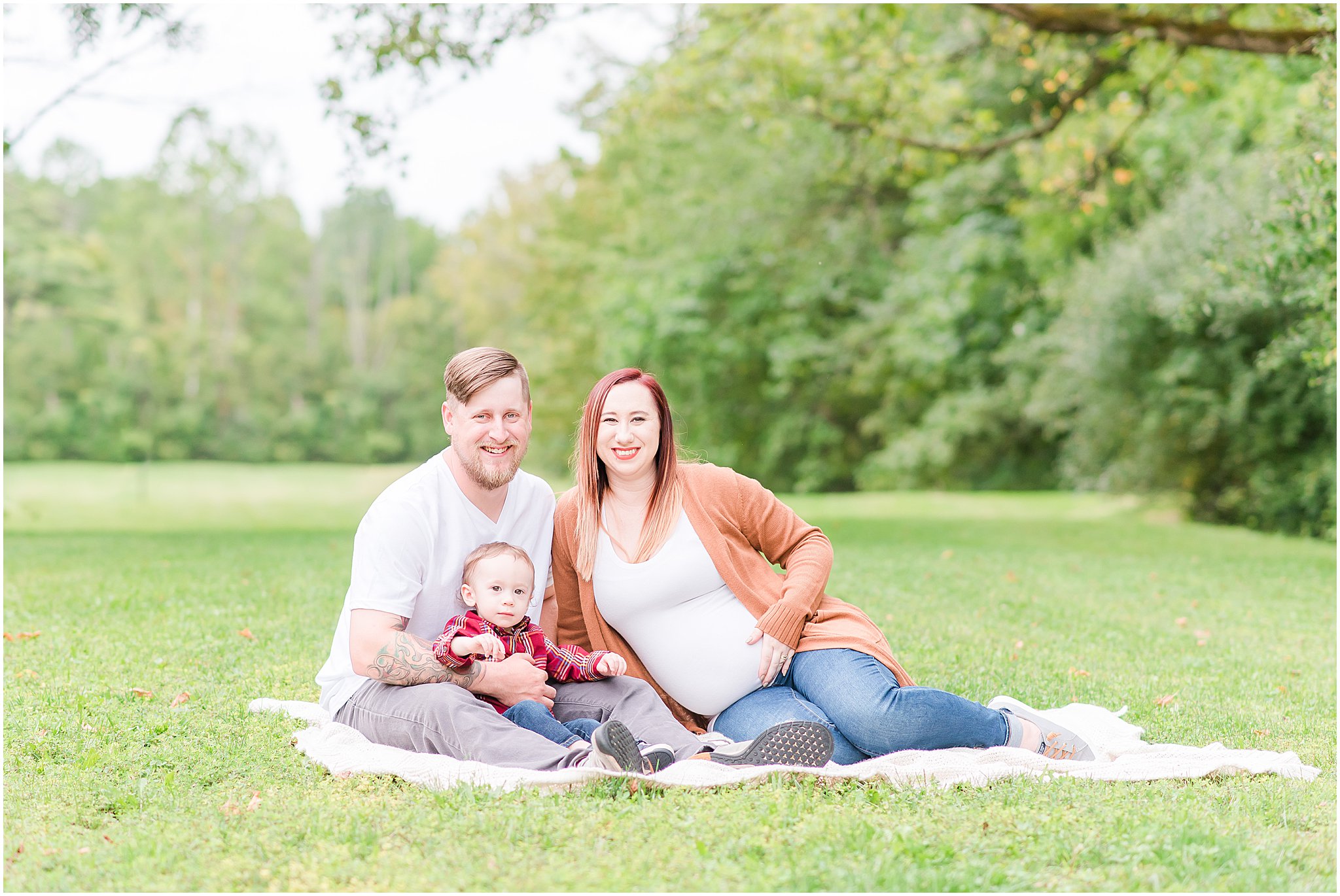 Family of three snuggled on blanket smiling at camera during Eagle Creek Park maternity session