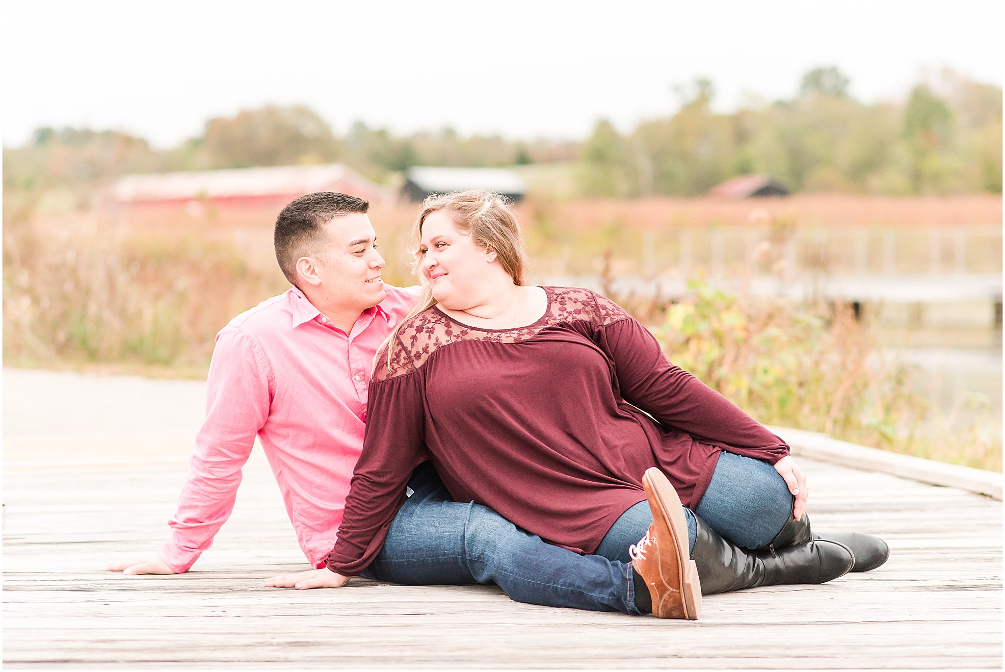 Couple sitting on dock and smiling at each other during Beckley Creek Park engagement session