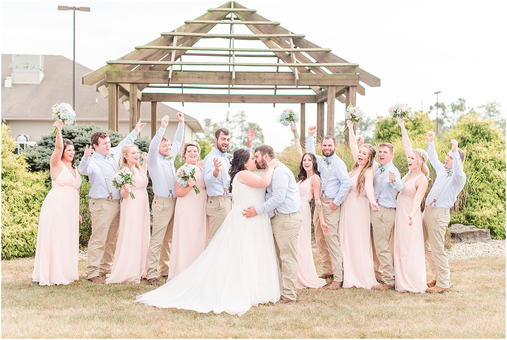 Bridal party cheering as bride and groom kiss during portraits at Cornerstone Hall in Salem, IN