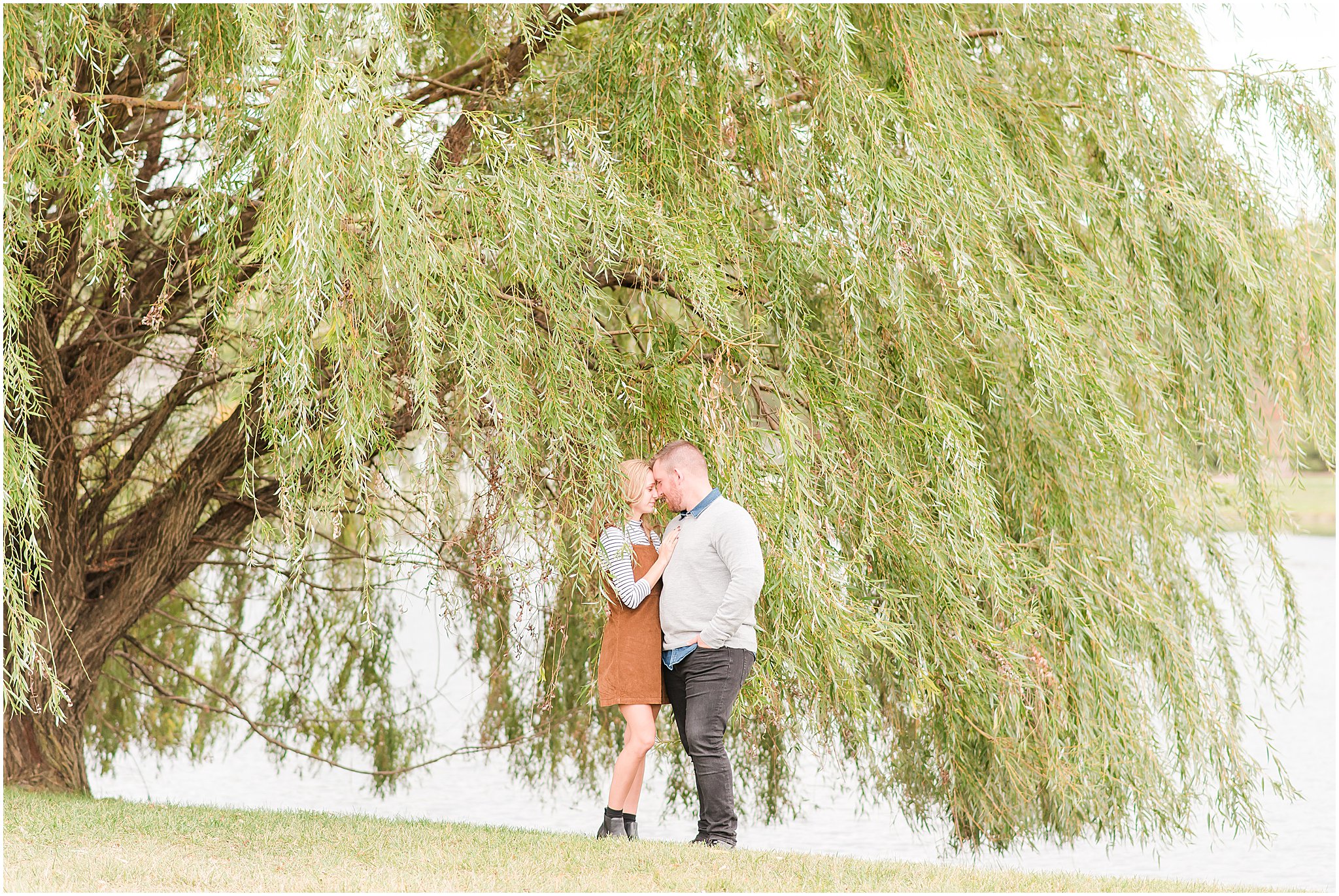 Couple nose to nose in front of willow tree during Coxhall Gardens engagement session