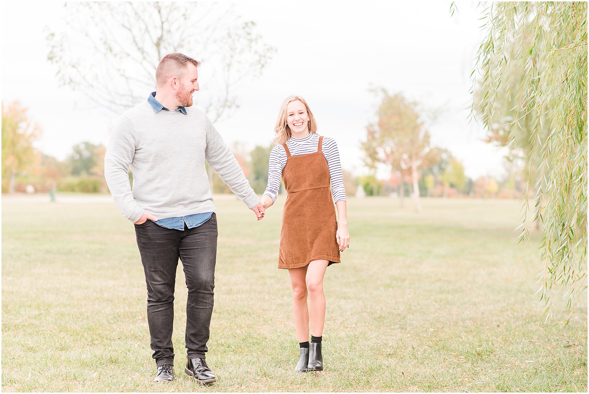 Couple holding hands and walking in front of willow tree during Coxhall Gardens engagement session