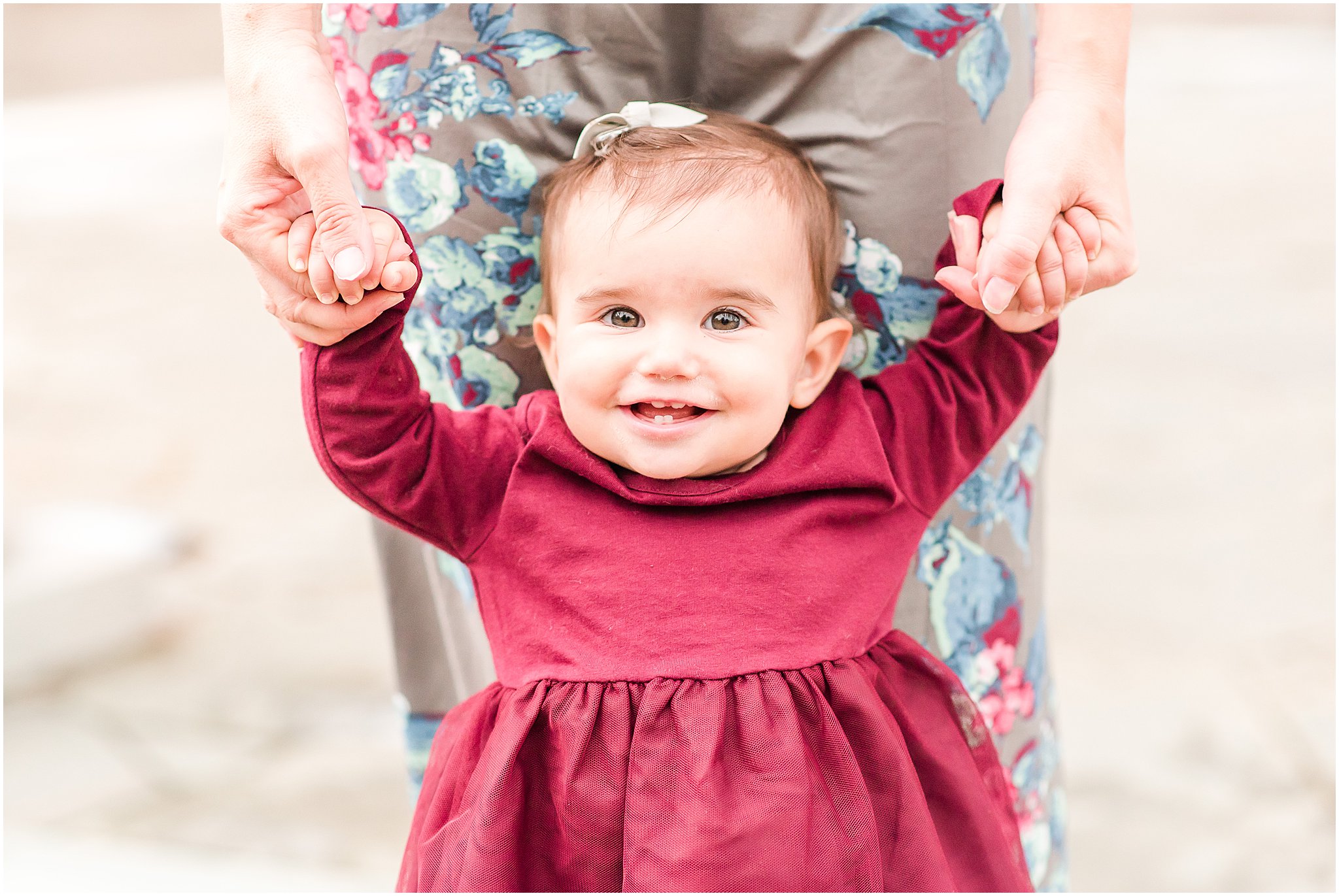 Toddler girl in burgundy dress grinning at camera during Coxhall Gardens family session