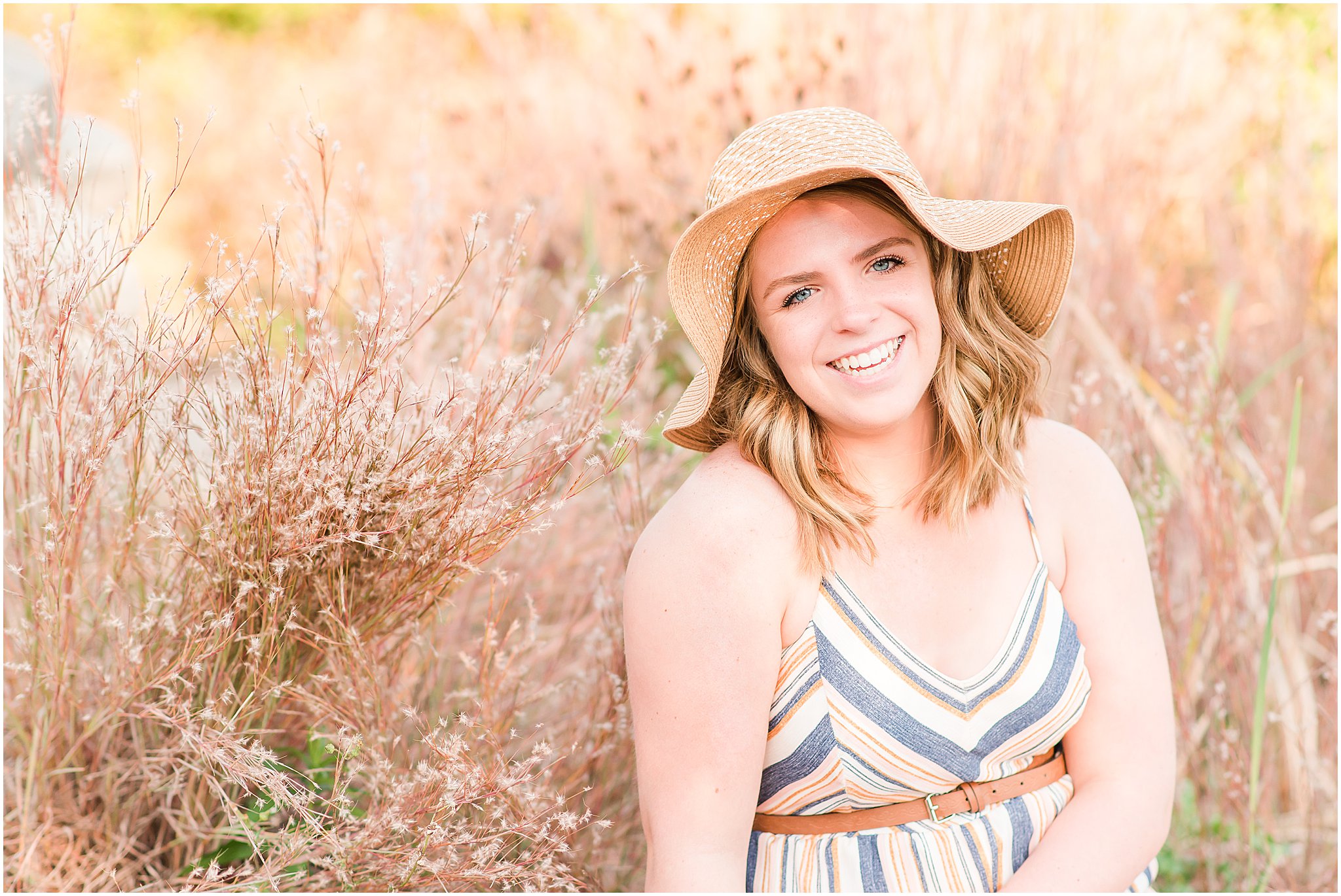 Girl with floppy tan hat laughing at camera during Coxhall Gardens senior session
