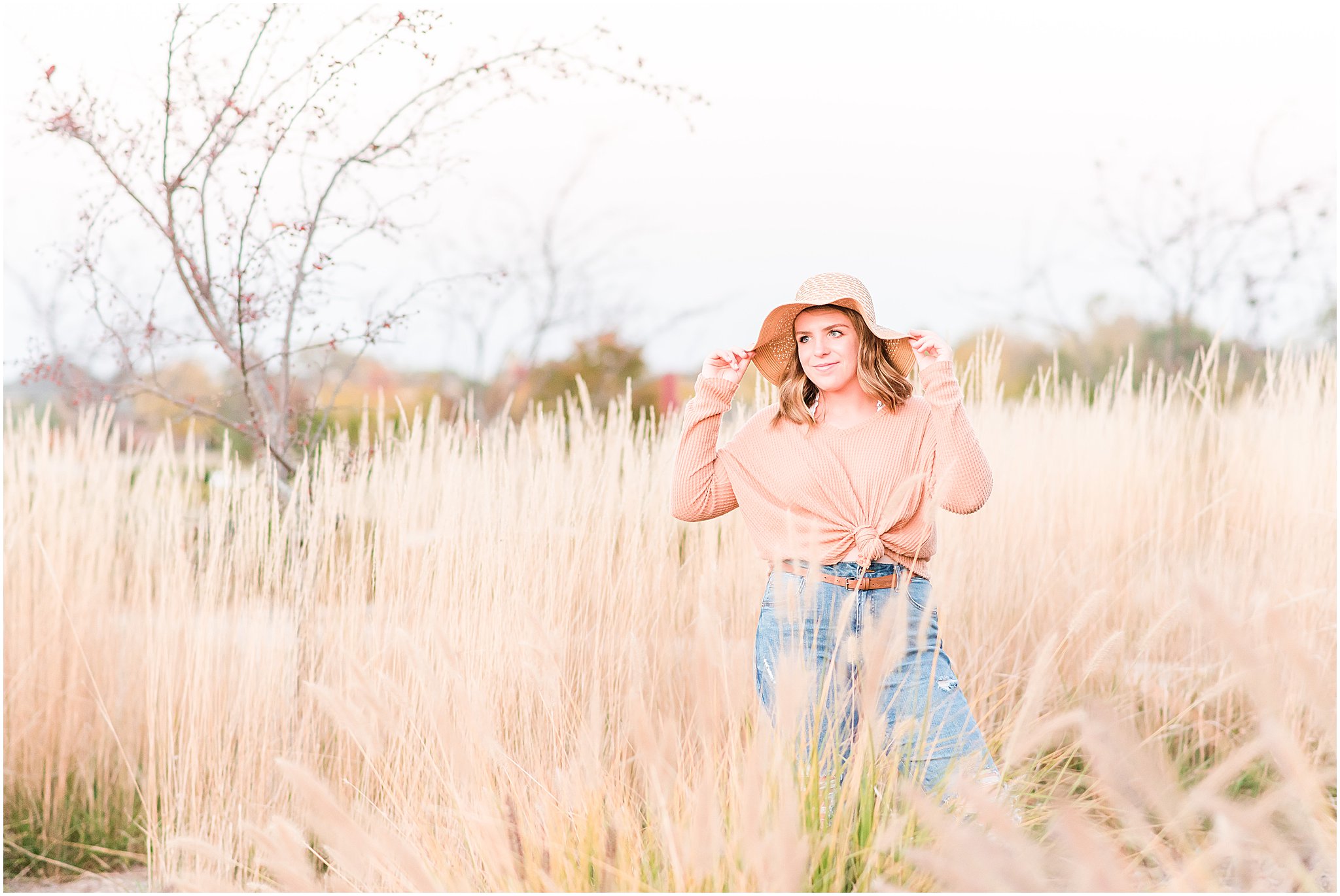 Girl in floppy tan hat in field smiling off camera during Coxhall Gardens senior session