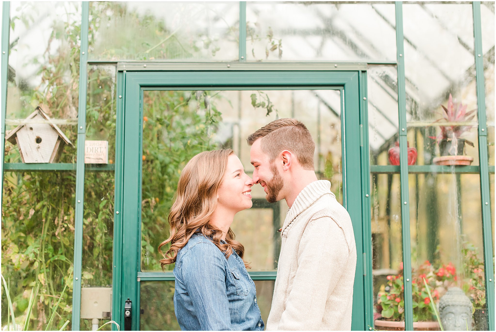 Couple nose to nose in front of green greenhouse at Defries Gardens