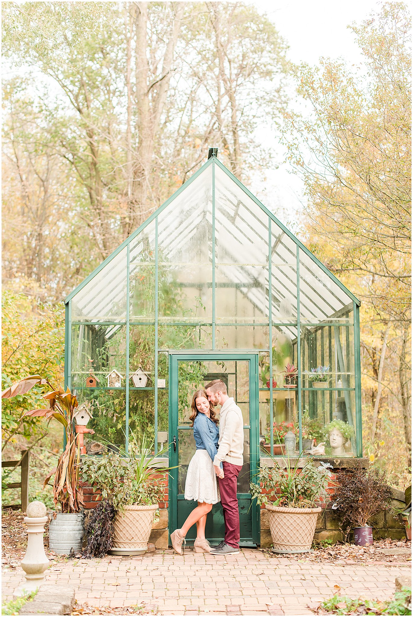 Couple nuzzling in front of green greenhouse at Defries Gardens