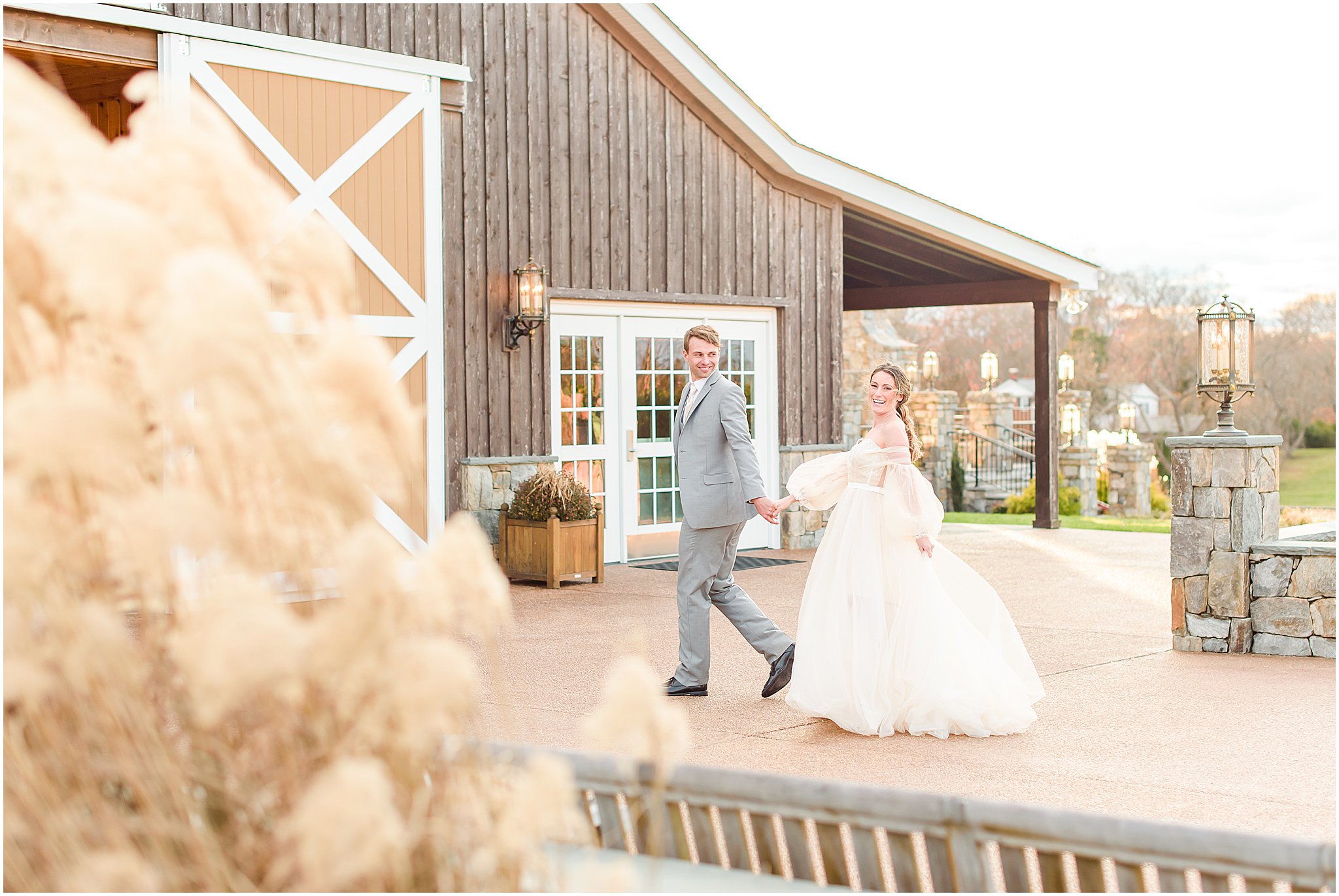 Bride and groom holding hands, walking and laughing in front of The Lodge at Mount Ida Farm