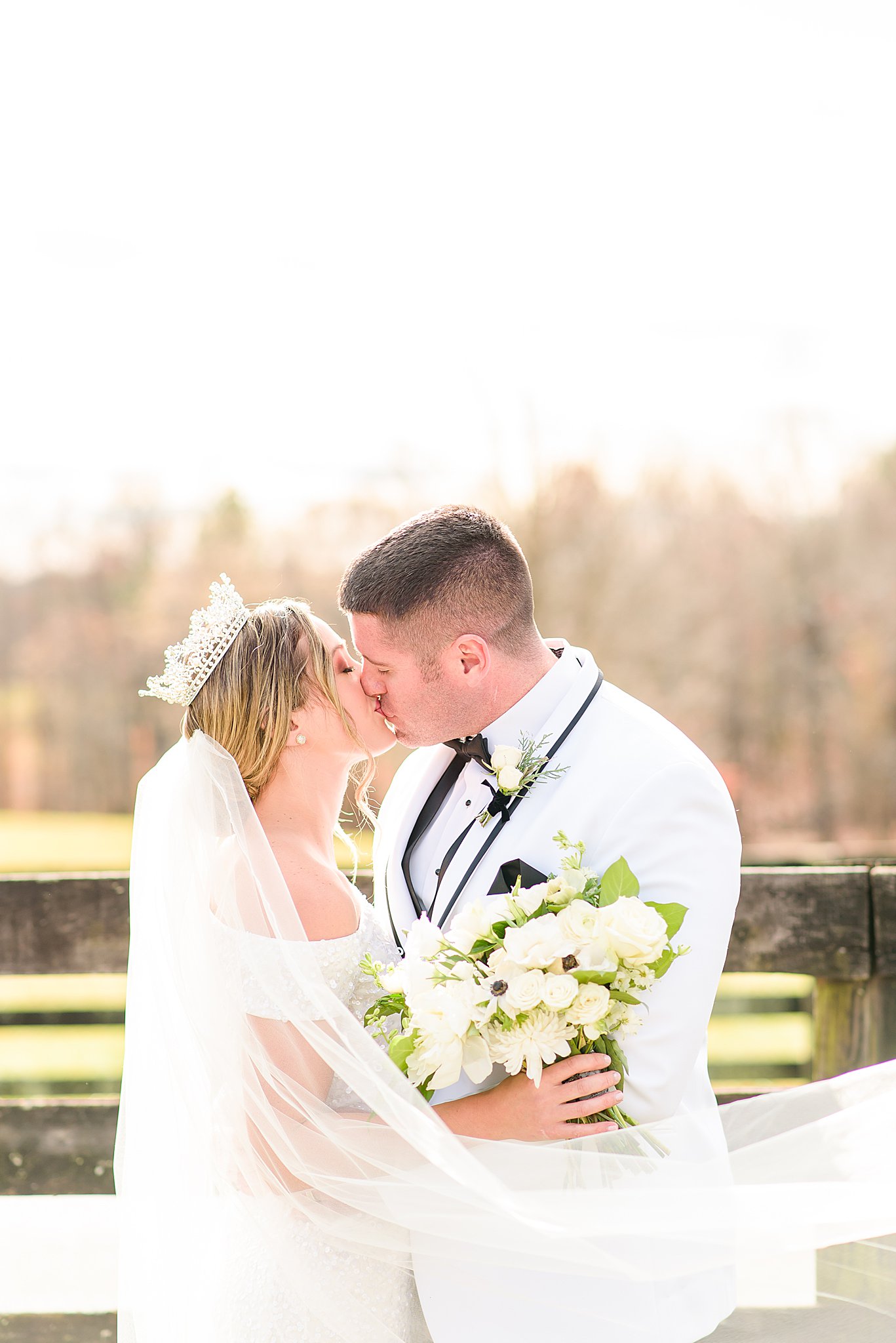 Bride and Groom kissing as veil blows around them in the wind at Mount Ida Farm wedding