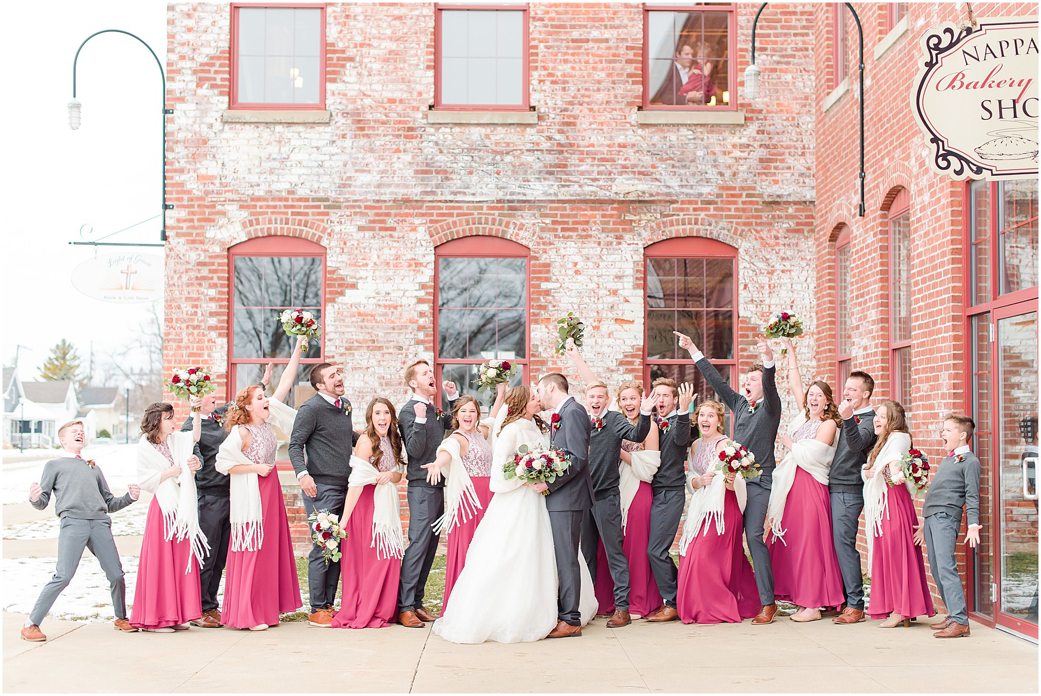 Bridal party in charcoal and berry colors cheering as Bride and Groom kiss Coppes Commons Wedding