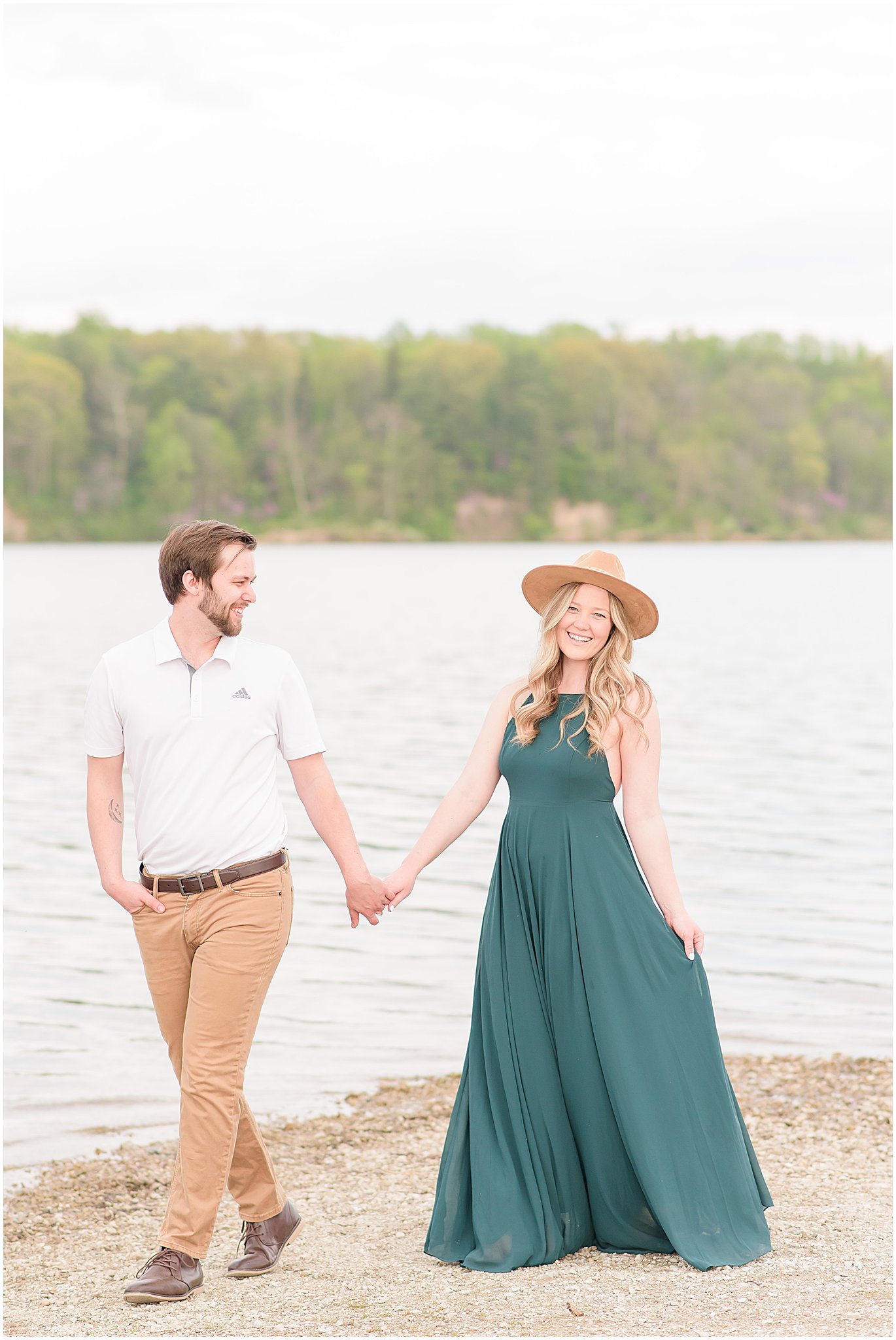 Couple holding hands and walking in front of lake during Eagle Creek Park Engagement Session