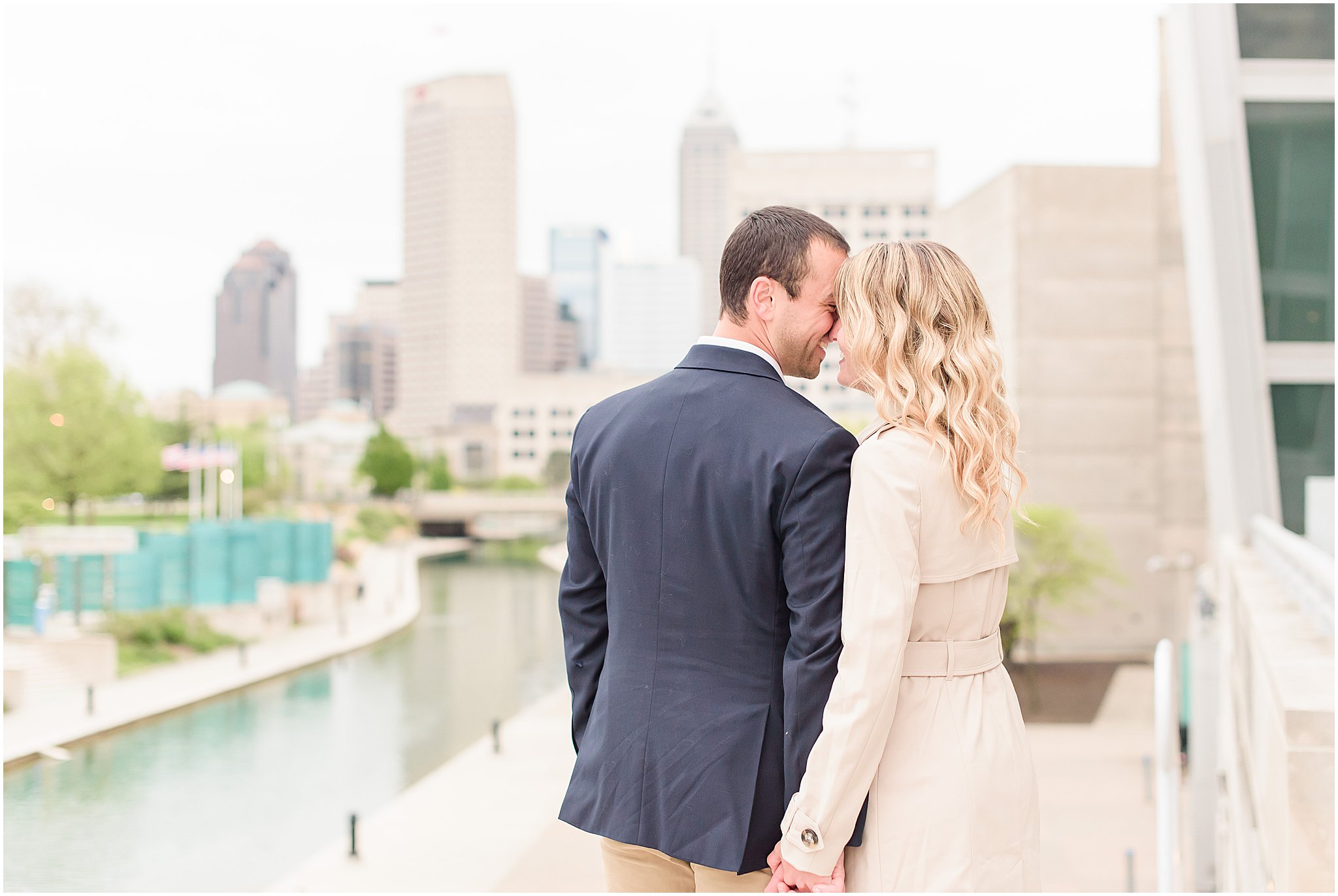 Couple nuzzling in front of Indy skyline during Indianapolis Canal engagement session 