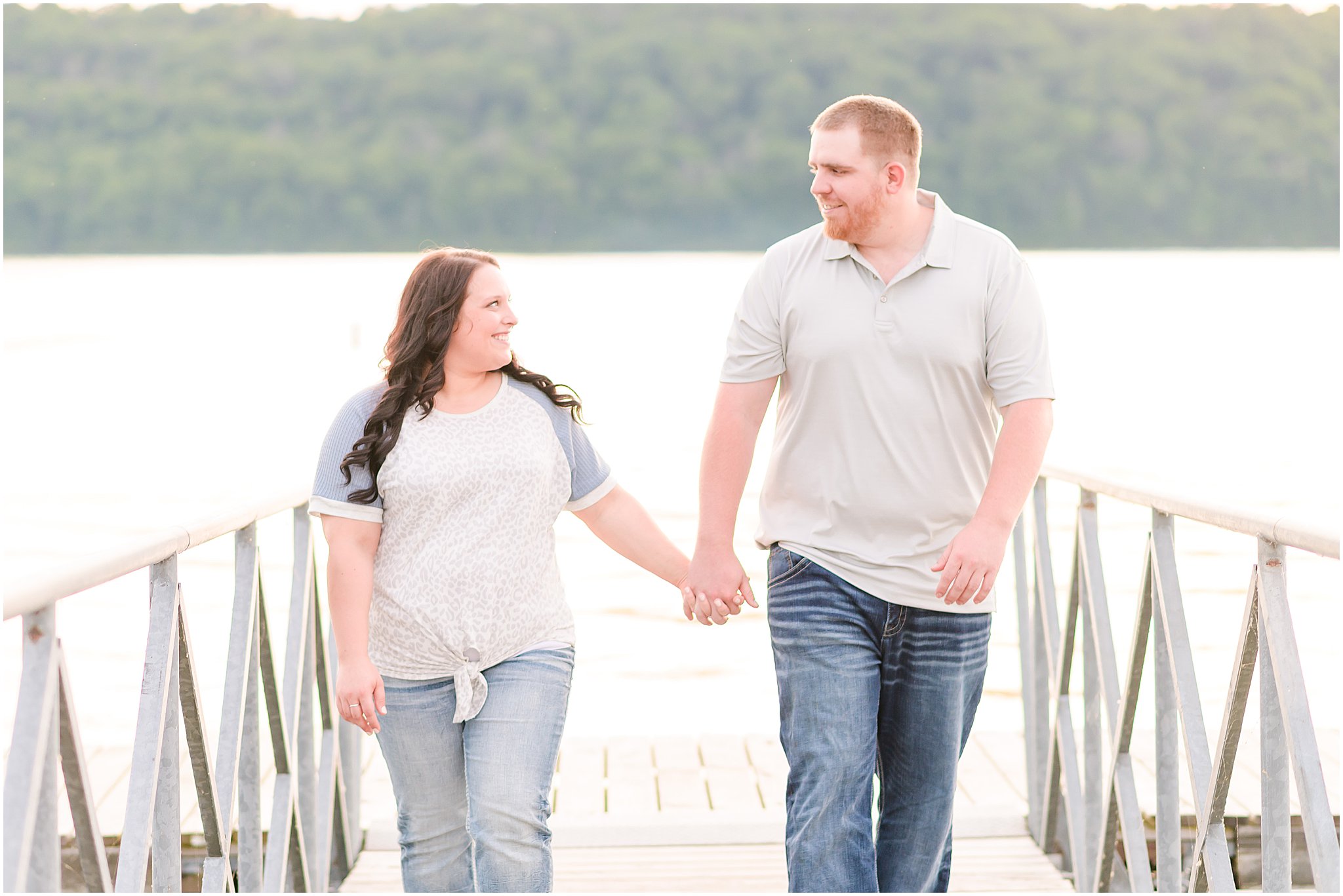 Couple holding hands and smiling walking on dock during Brookville Lake engagement session