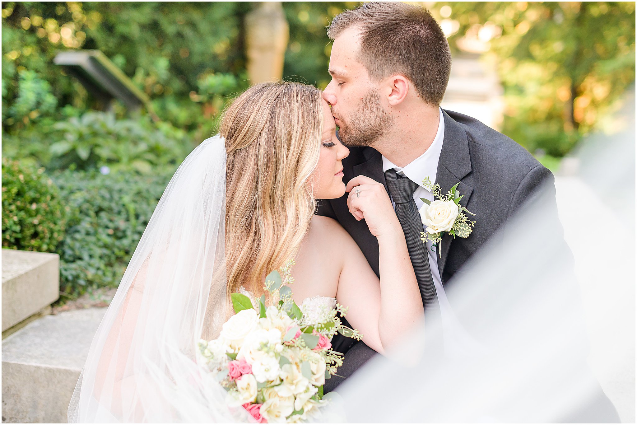 Groom kissing bride's forehead veil swoop Newfields summer wedding