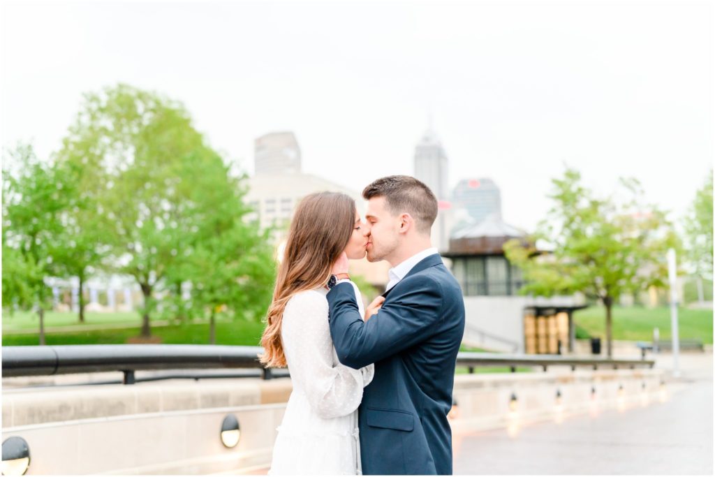 Couple kissing with Indy skyline in background downtown Indianapolis canal engagement session