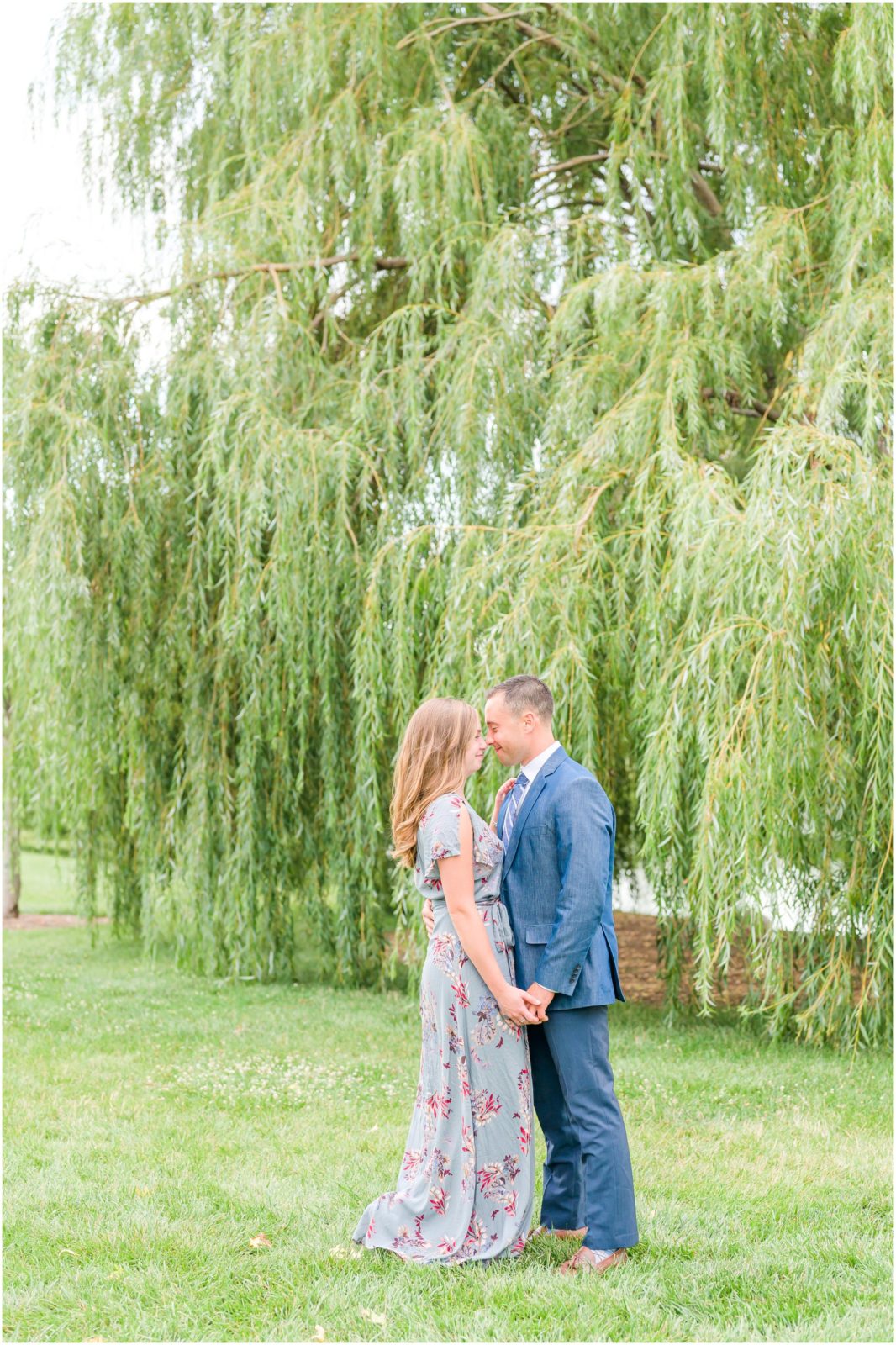 Couple standing nose to nose in front of willow tree Coxhall Gardens engagement session