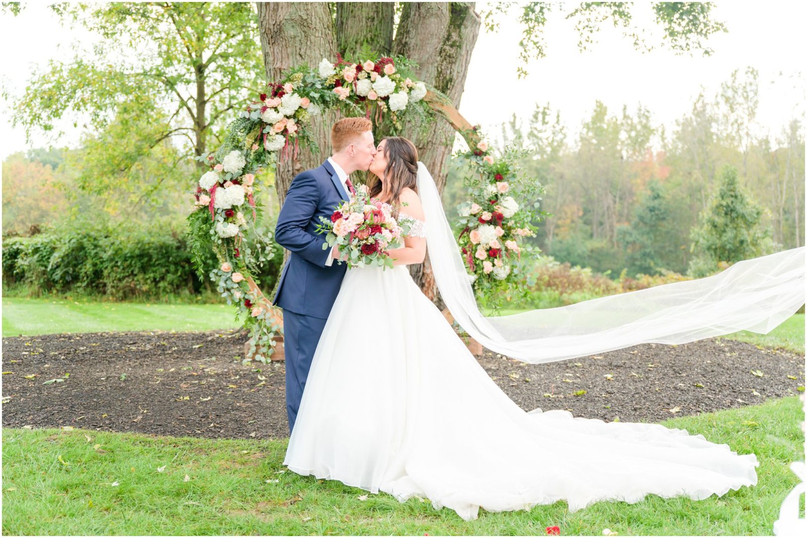 Dip kiss in front of floral arch Mustard Seed Gardens wedding