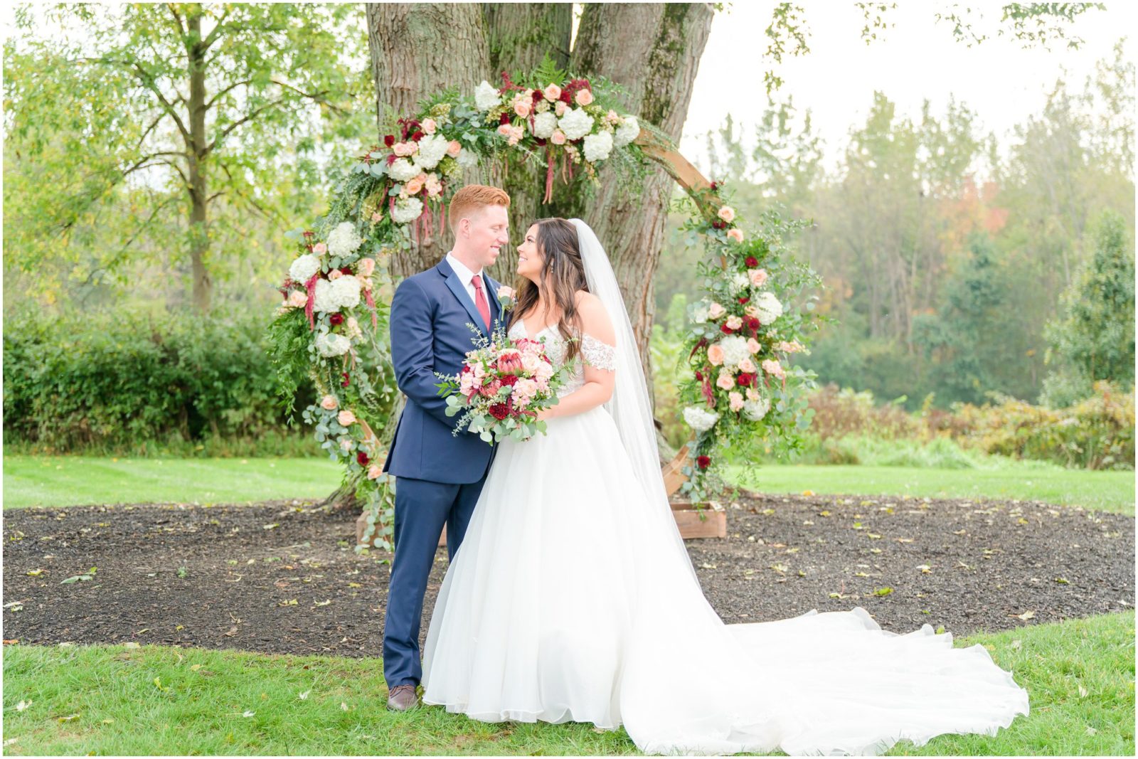 Bride and groom smiling at each other in front of floral arch Mustard Seed Gardens wedding