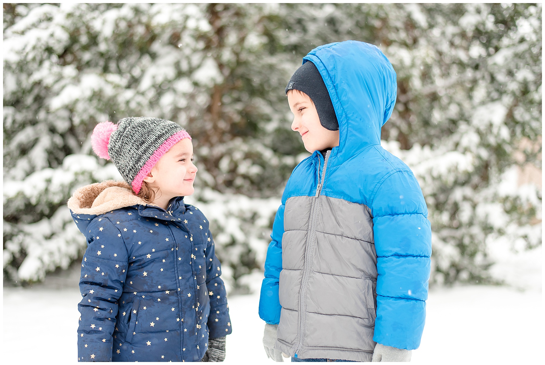Boy in blue coat and girl in navy coat smiling at each other out in the snow