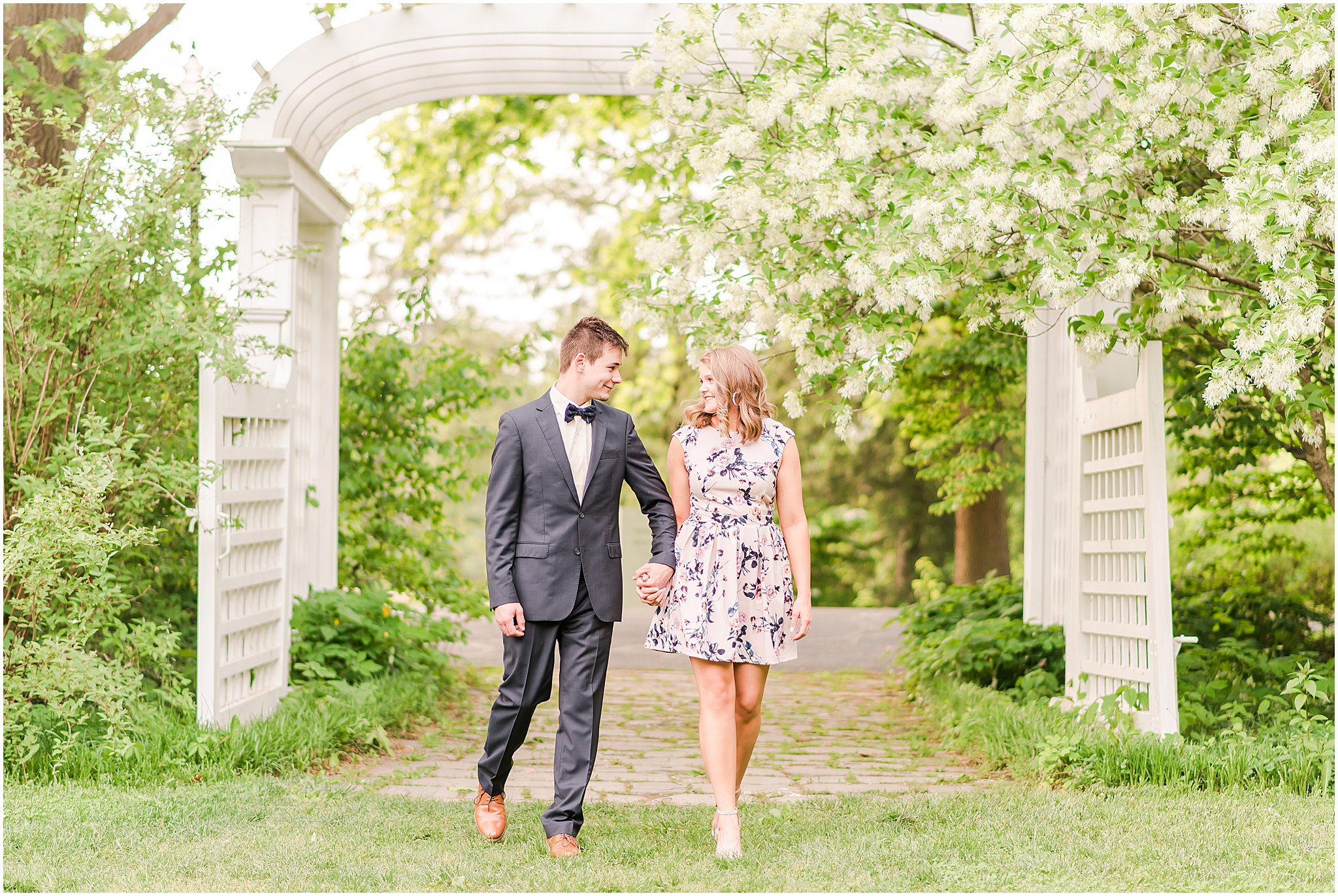 Boy and girl holding handing and walking under an arch at Newfields engagement session sporting fun spring fashion trends
